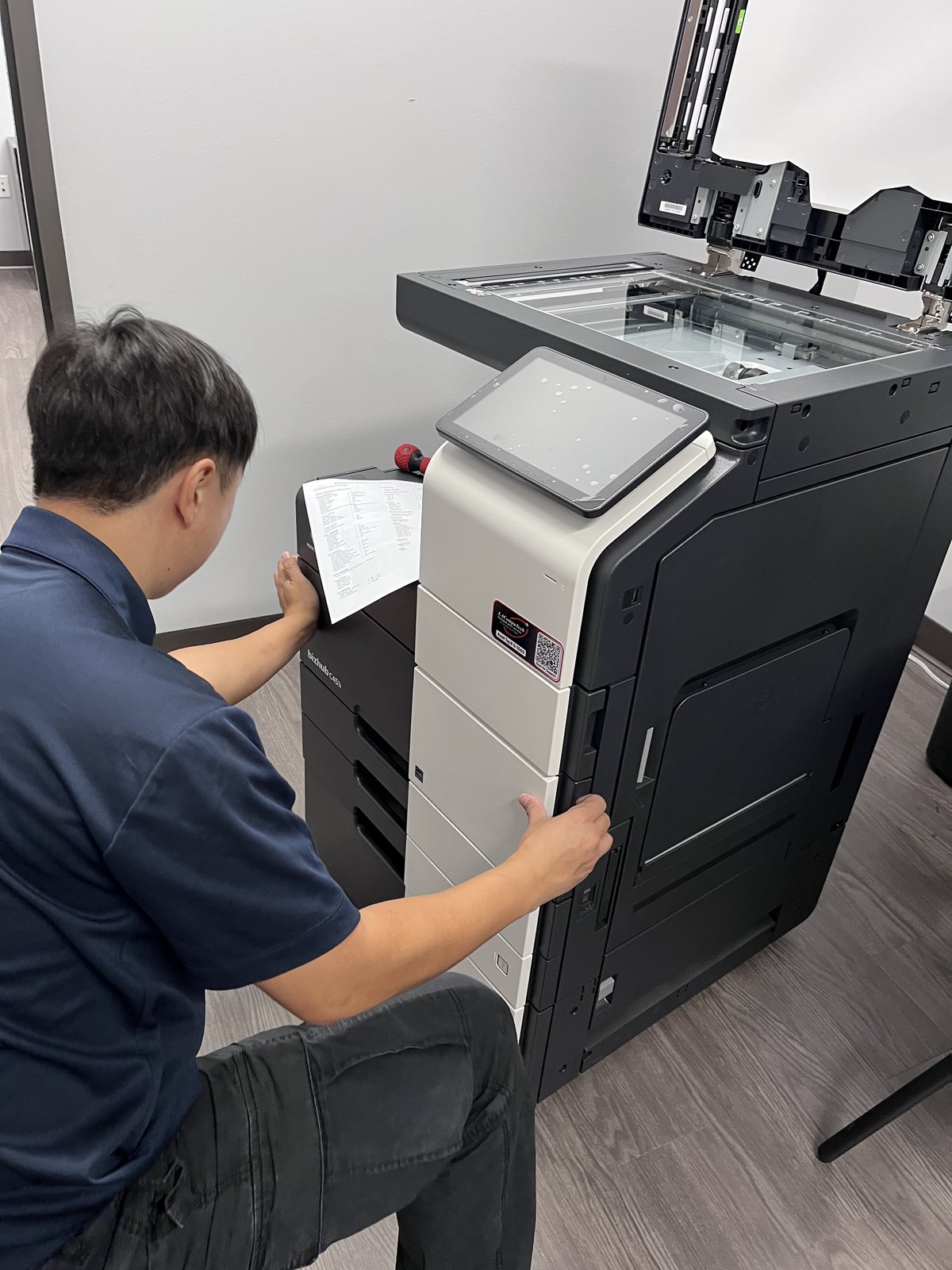 An LAComputech technician servicing a Konica Minolta bizhub multifunction printer